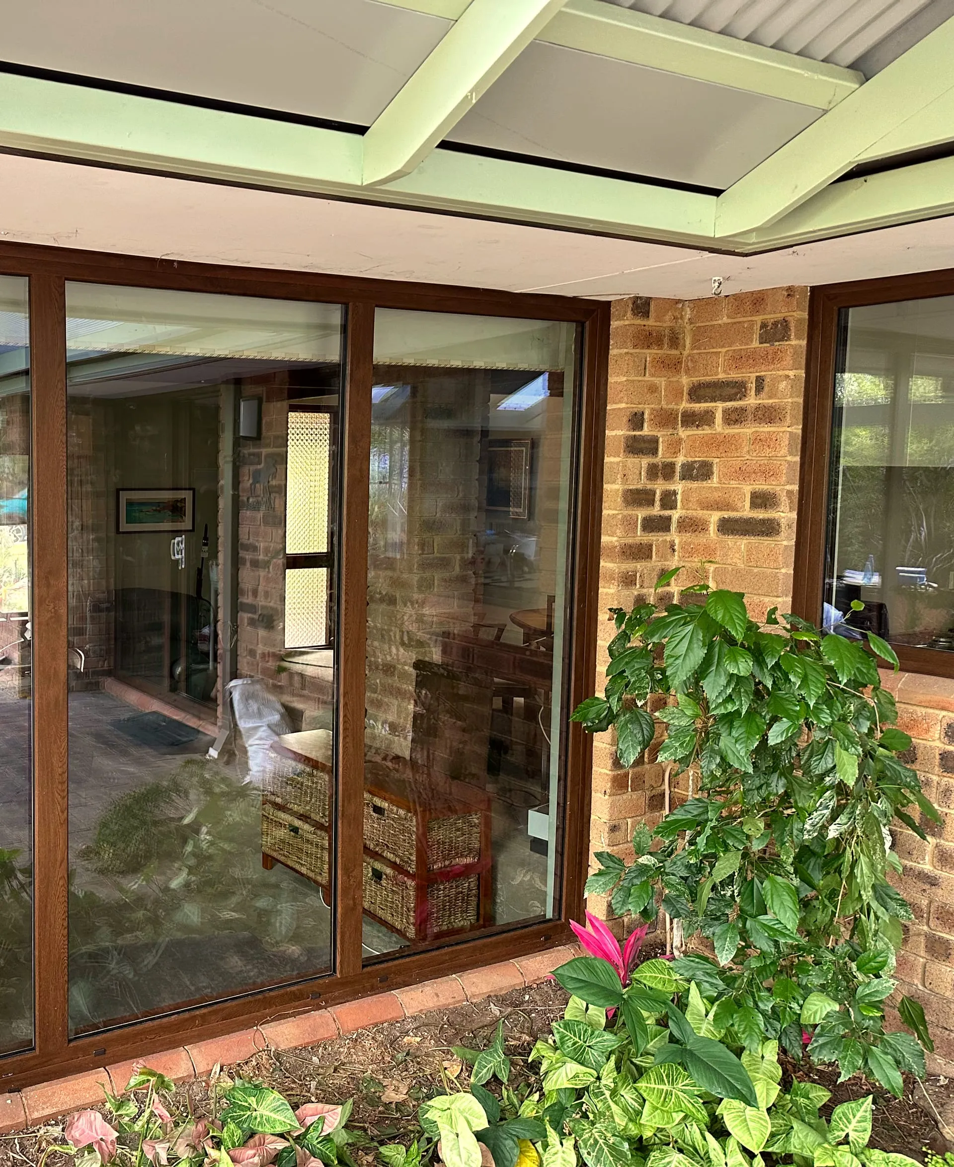 Golden-oak woodgrain uPVC sliding door and corner window under an alfresco roof, seen from the garden — GaBe Double Glazing install, Perth