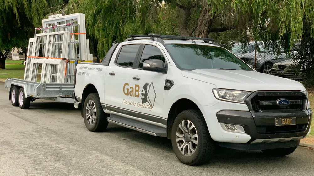 A GaBe Double Glazing branded ute towing a trailer of uPVC window and door frames to a job, Perth