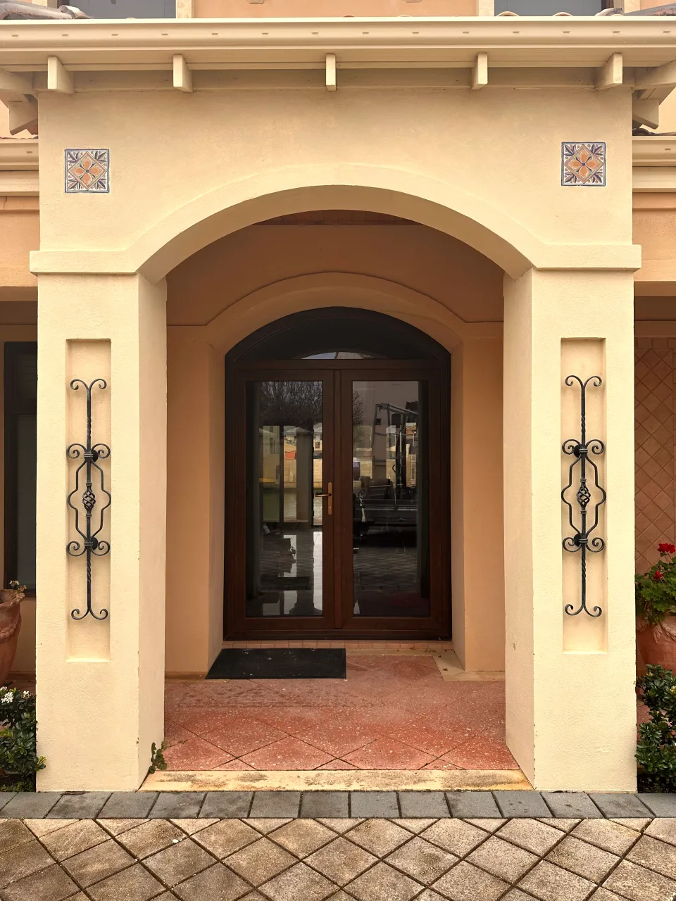 Arched dark-timber-look double entrance door under a Mediterranean-style stucco porch