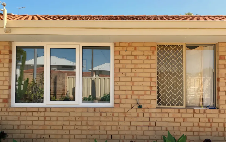 White retrofit windows in beige brick beside an older security screen